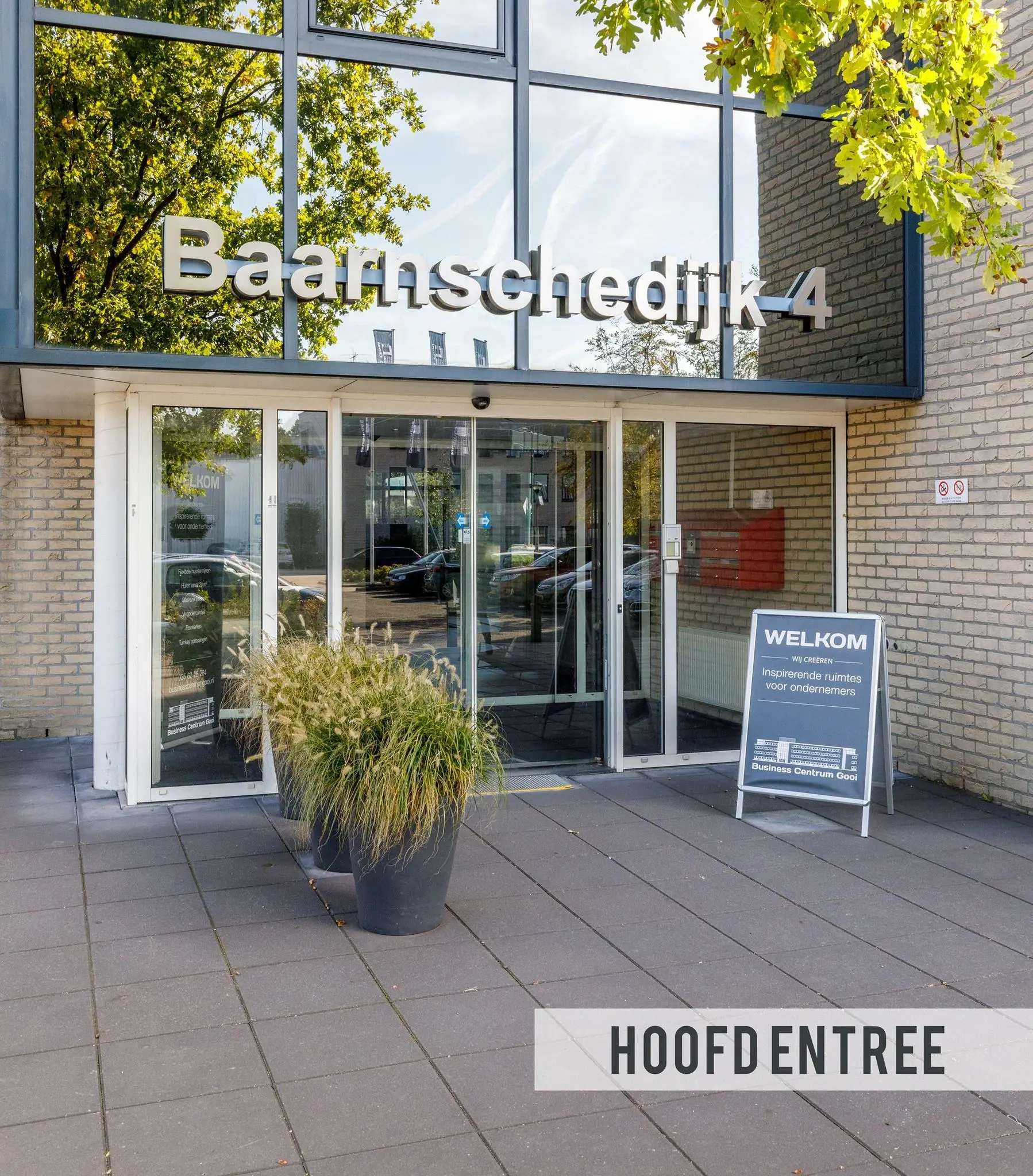 Hoofdentree van het gebouw aan de Baarnsche Dijk 4 met glazen deuren en een welkomstbord voor ondernemers.